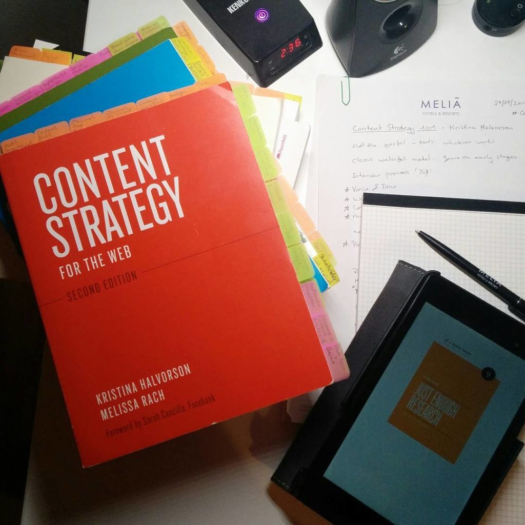 Piles de livres sur la stratégie de contenu avec des post-its qui dépassent, des notes de conférences et d'autres objets installant une ambiance studieuse posés sur un bureau